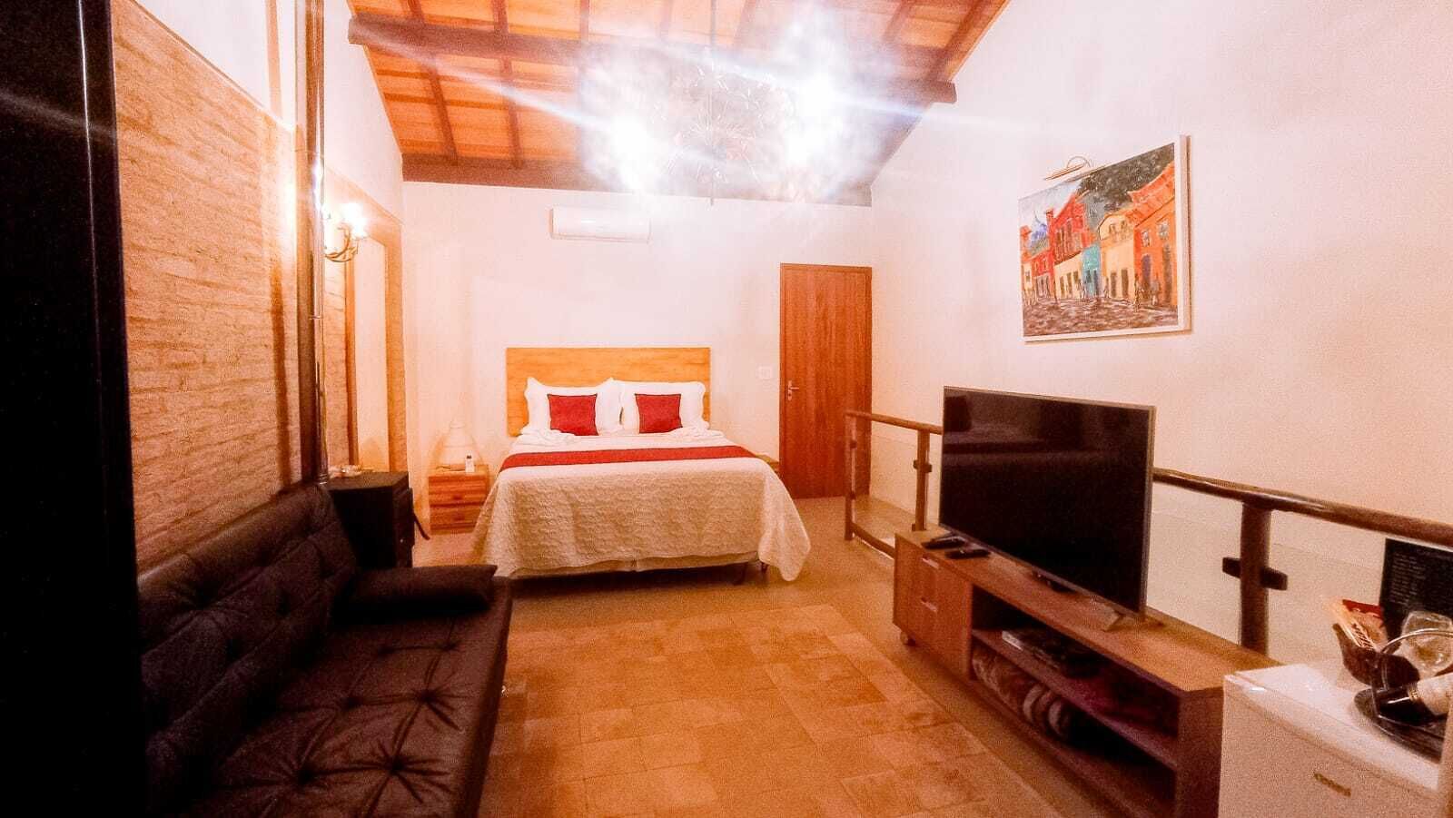 Un dormitorio con cama, televisión, sofá y un cuadro en la pared.