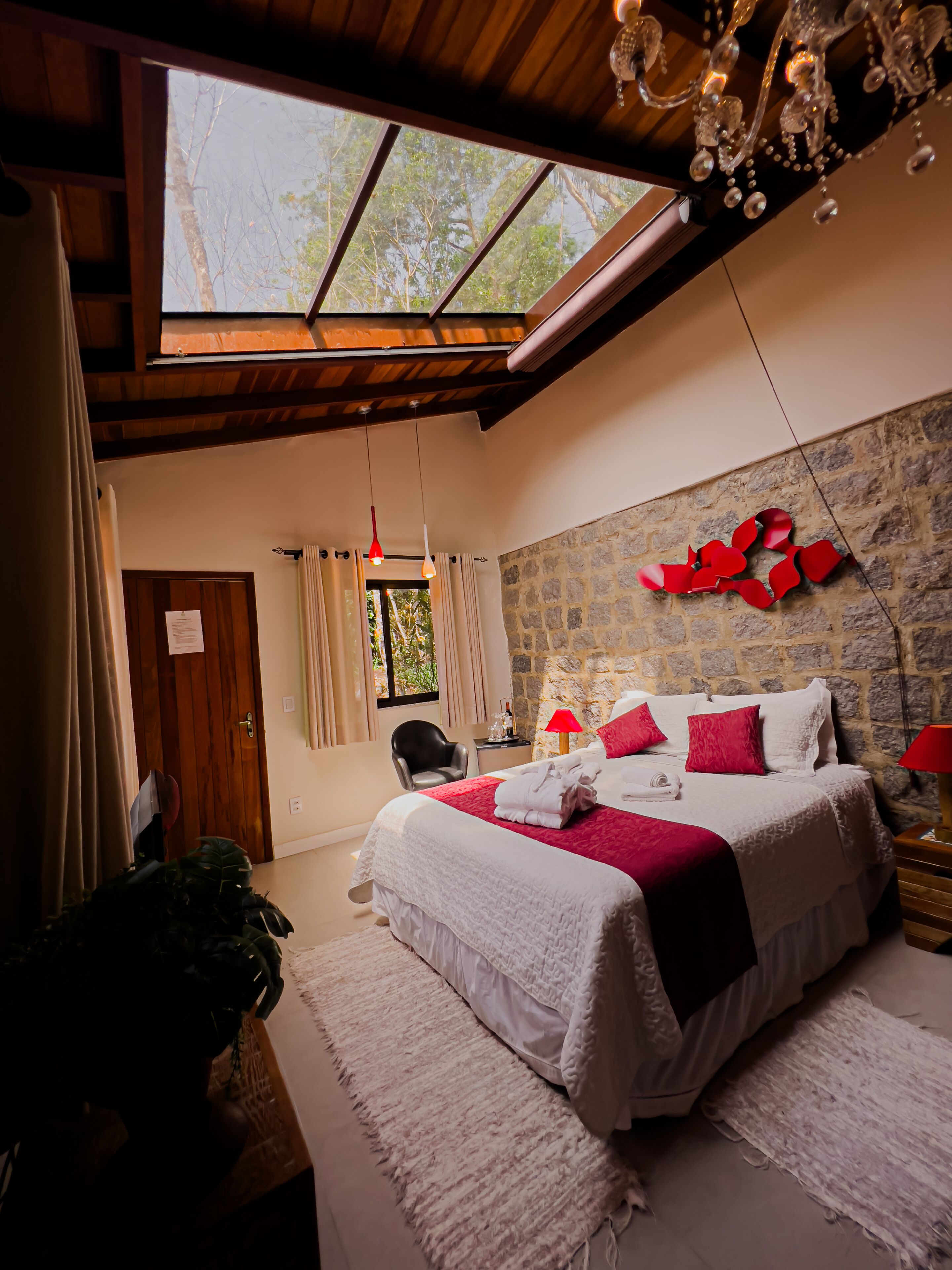 A bedroom with a large bed, a stone wall, a skylight, and a chandelier.
