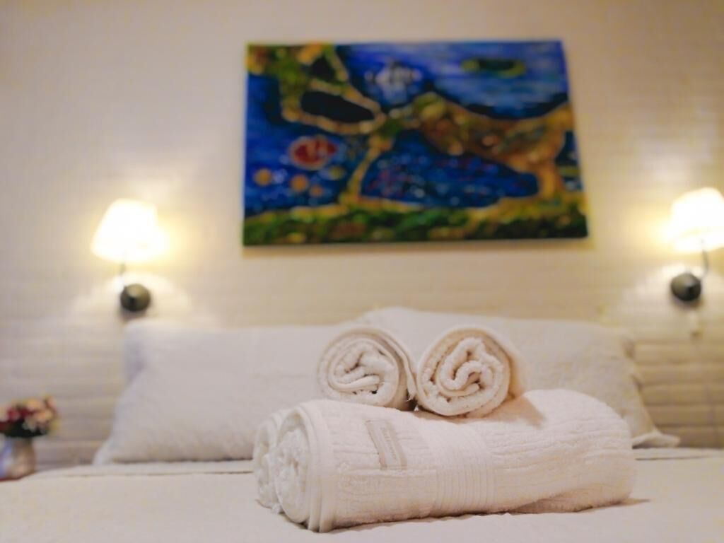 A neatly made bed with rolled towels and a painting on the wall.