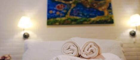 A neatly made bed with rolled towels and a painting on the wall.