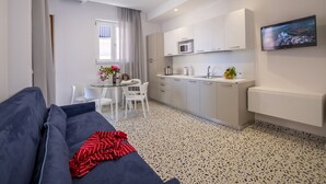 A compact living space with a sofa, a dining table with chairs, a kitchenette, and a TV mounted on the wall. - Neva-Elegant Suite with Balcony in Massa Lubrense center 10 minutes from Sorrento (Massa Lubrense)