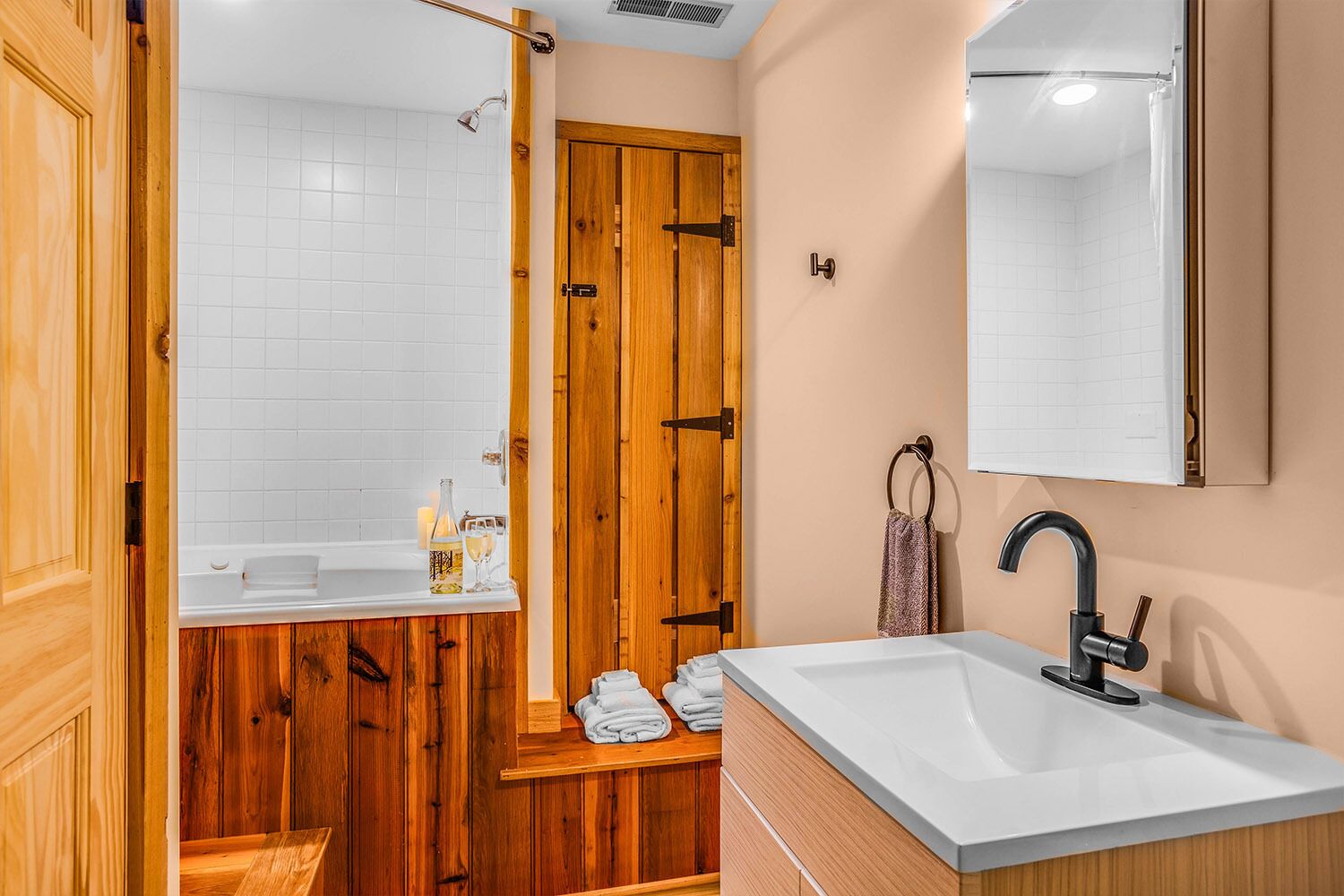 A bathroom with a wooden vanity, a sink, a mirror, and a shower area.