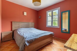 A bedroom with a wooden bed, a nightstand, a window with a view, and a wooden bench.