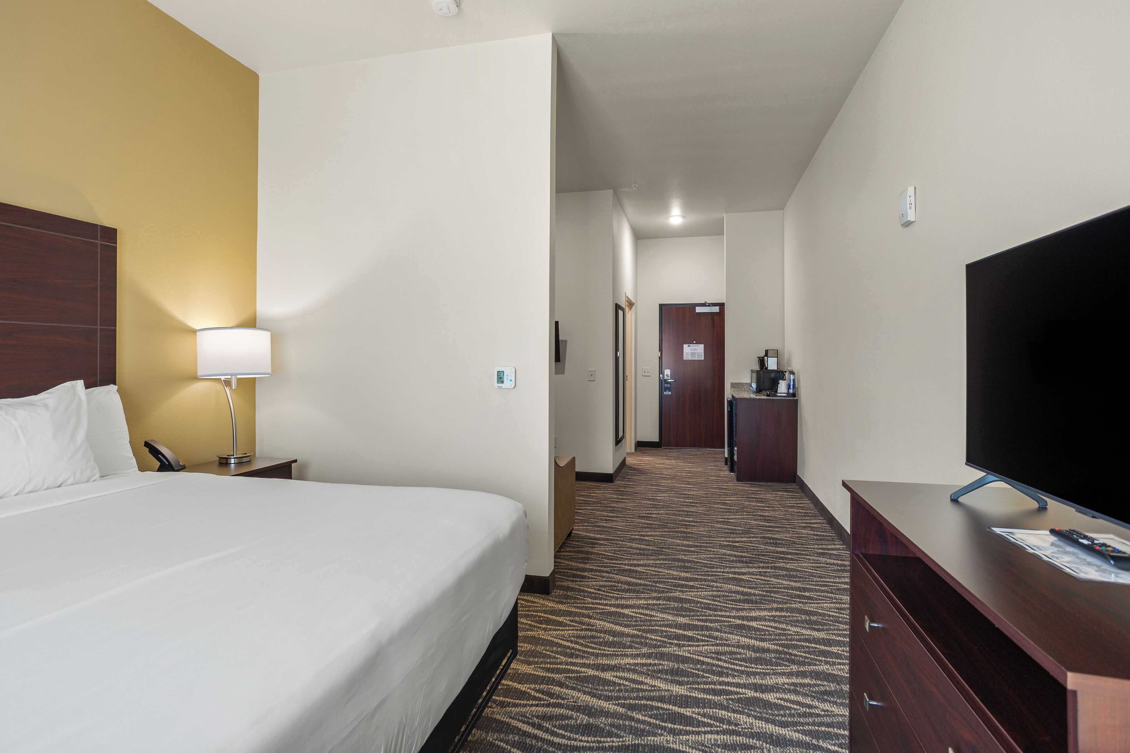 A hotel room with a large bed, a desk with a flat-screen TV, a lamp, and a carpeted floor.