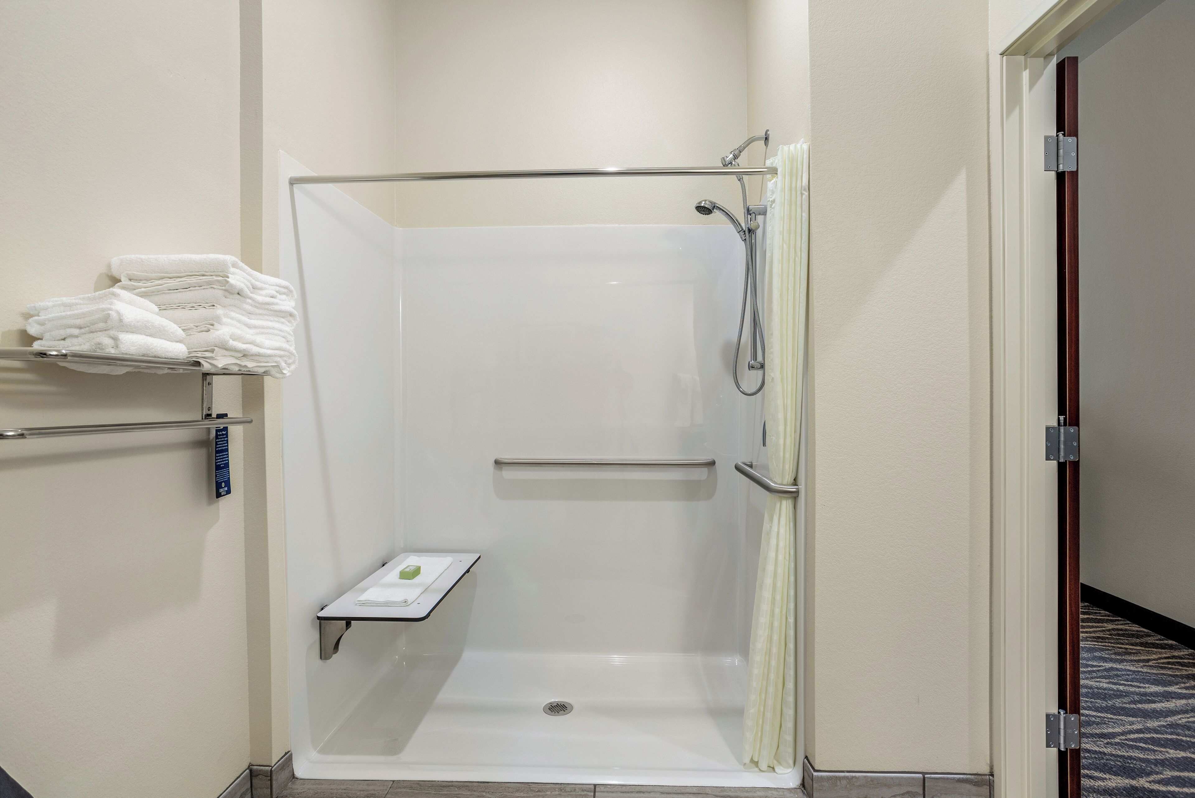 A walk-in shower with a glass door, a towel rack with folded towels, and a small shelf with toiletries.