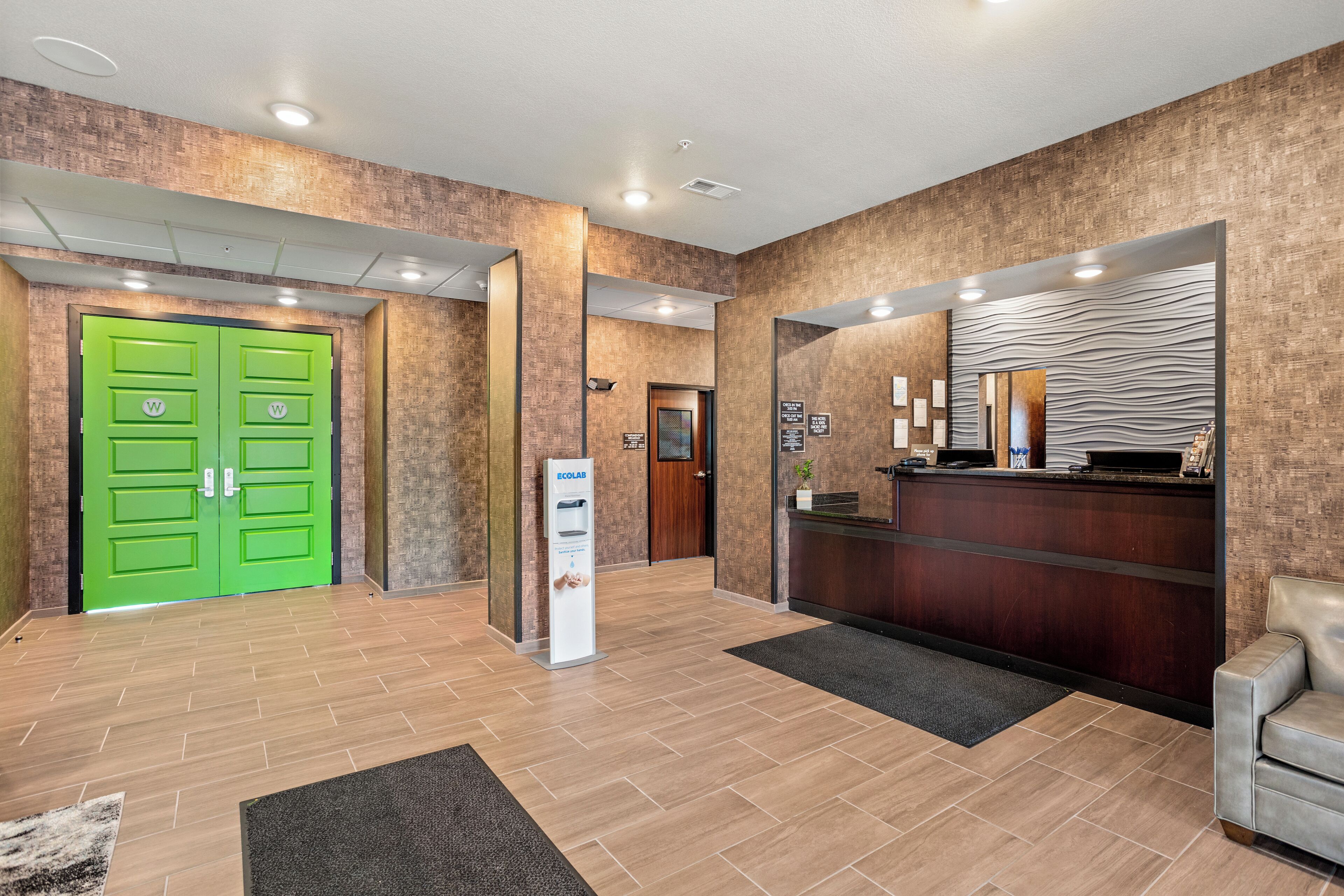 A hotel lobby with a reception desk, a green double door, and a reception area with a counter and a mirror.