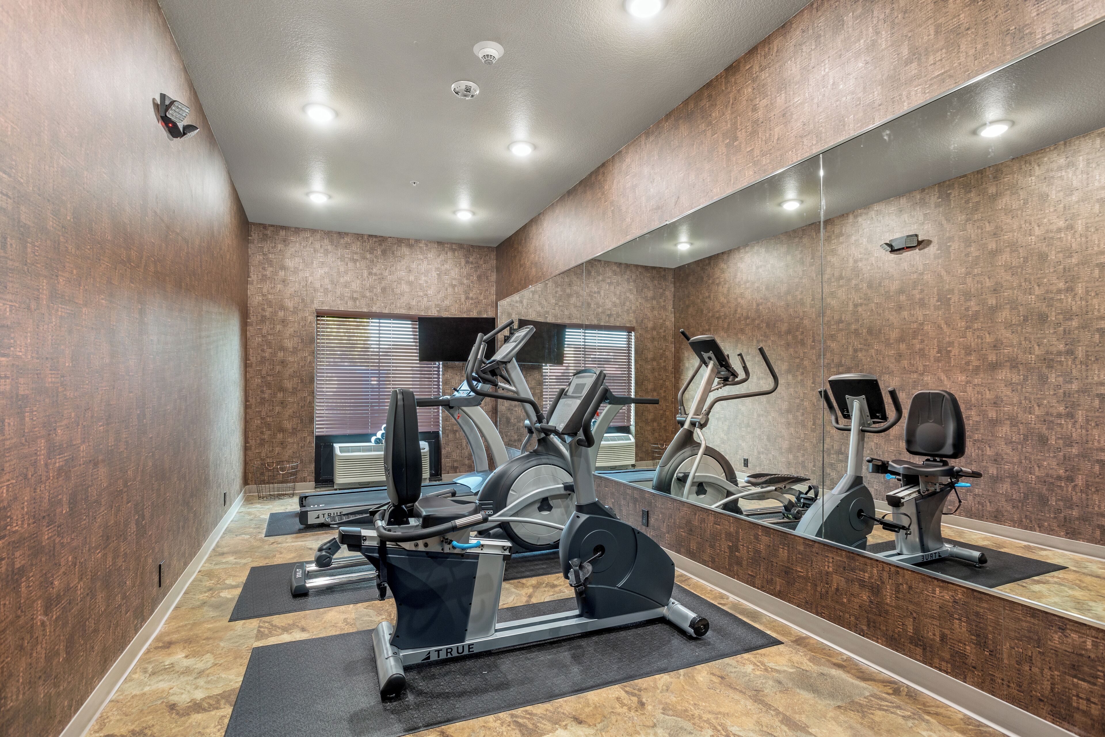 A gym with exercise equipment, a large mirror, and a window with blinds.