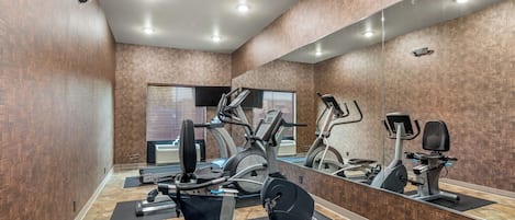A gym with exercise equipment, a large mirror, and a window with blinds.