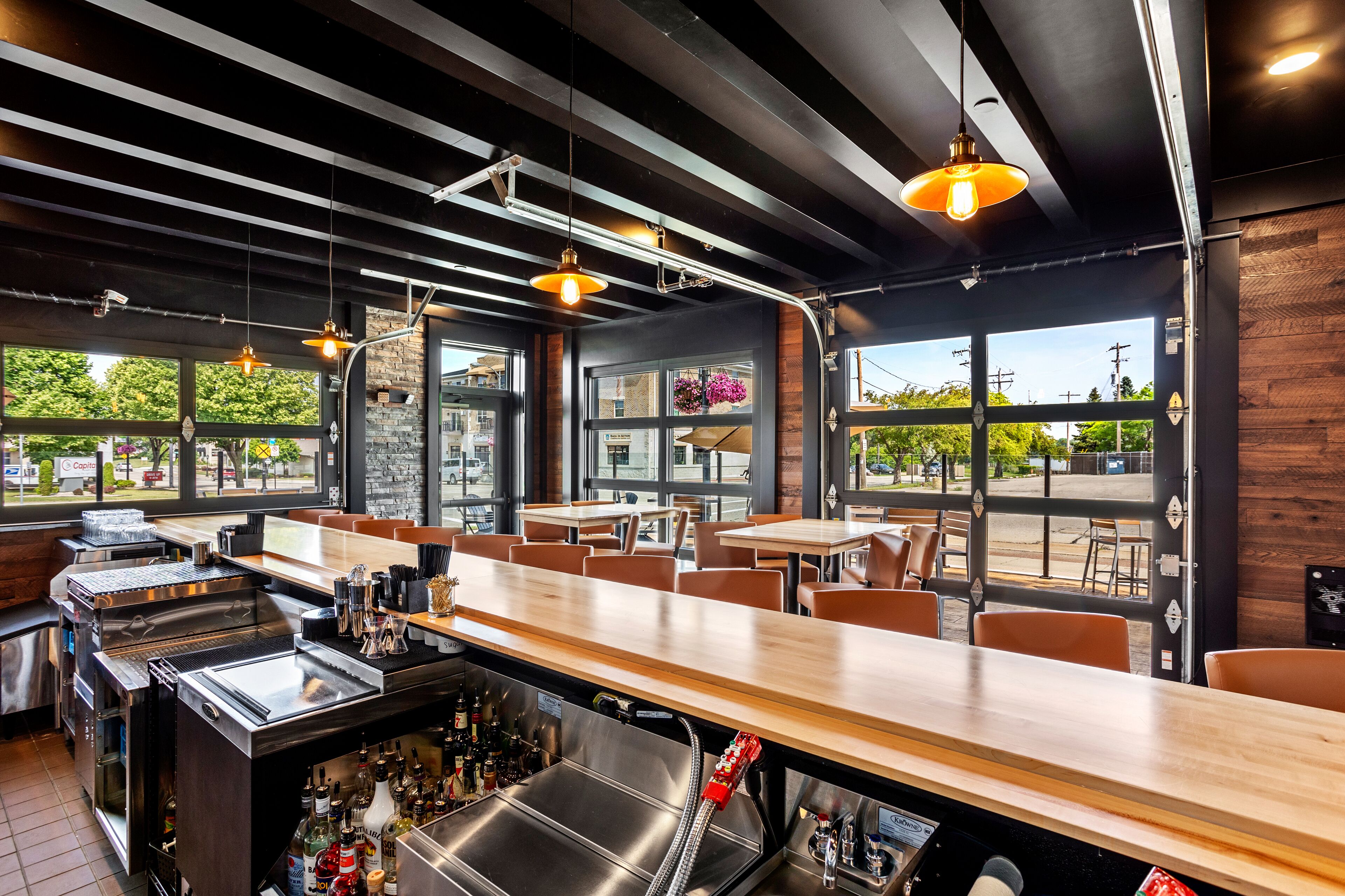 A restaurant interior with a bar area, seating, and large windows offering outdoor views.
