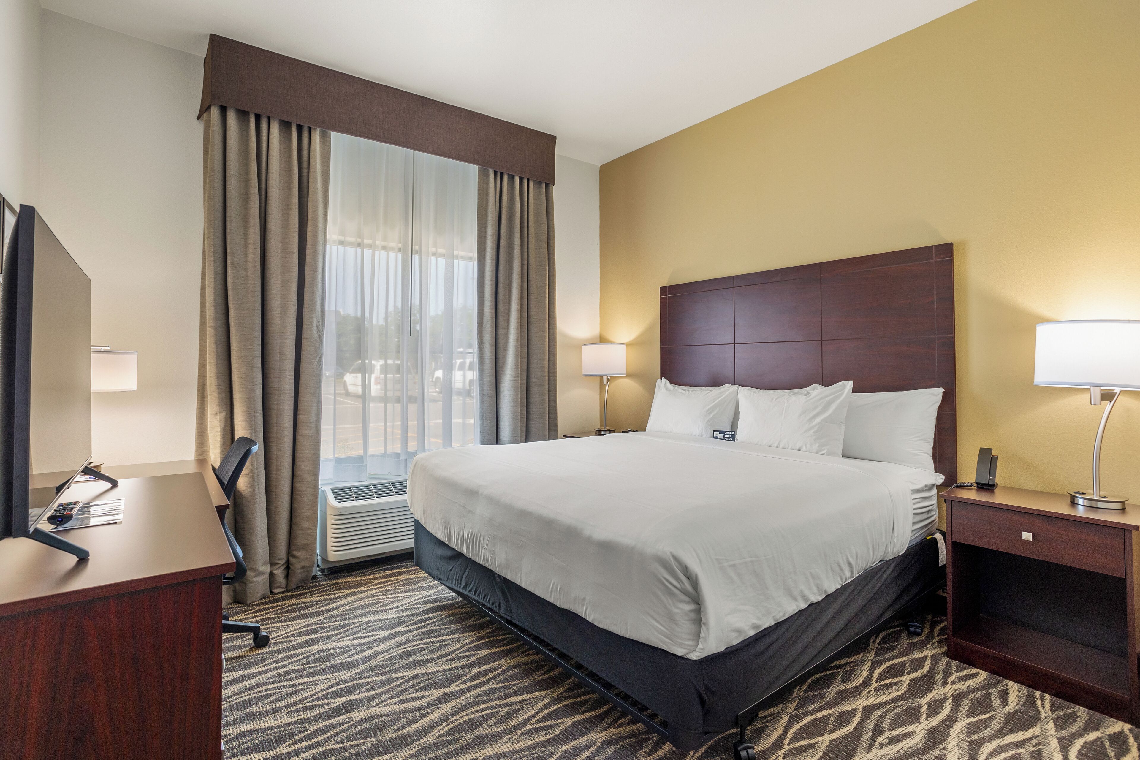 Ein Hotelzimmer mit einem großen Bett, einem Schreibtisch, einem Sessel, einem Nachttisch und einem Fenster mit Vorhängen.