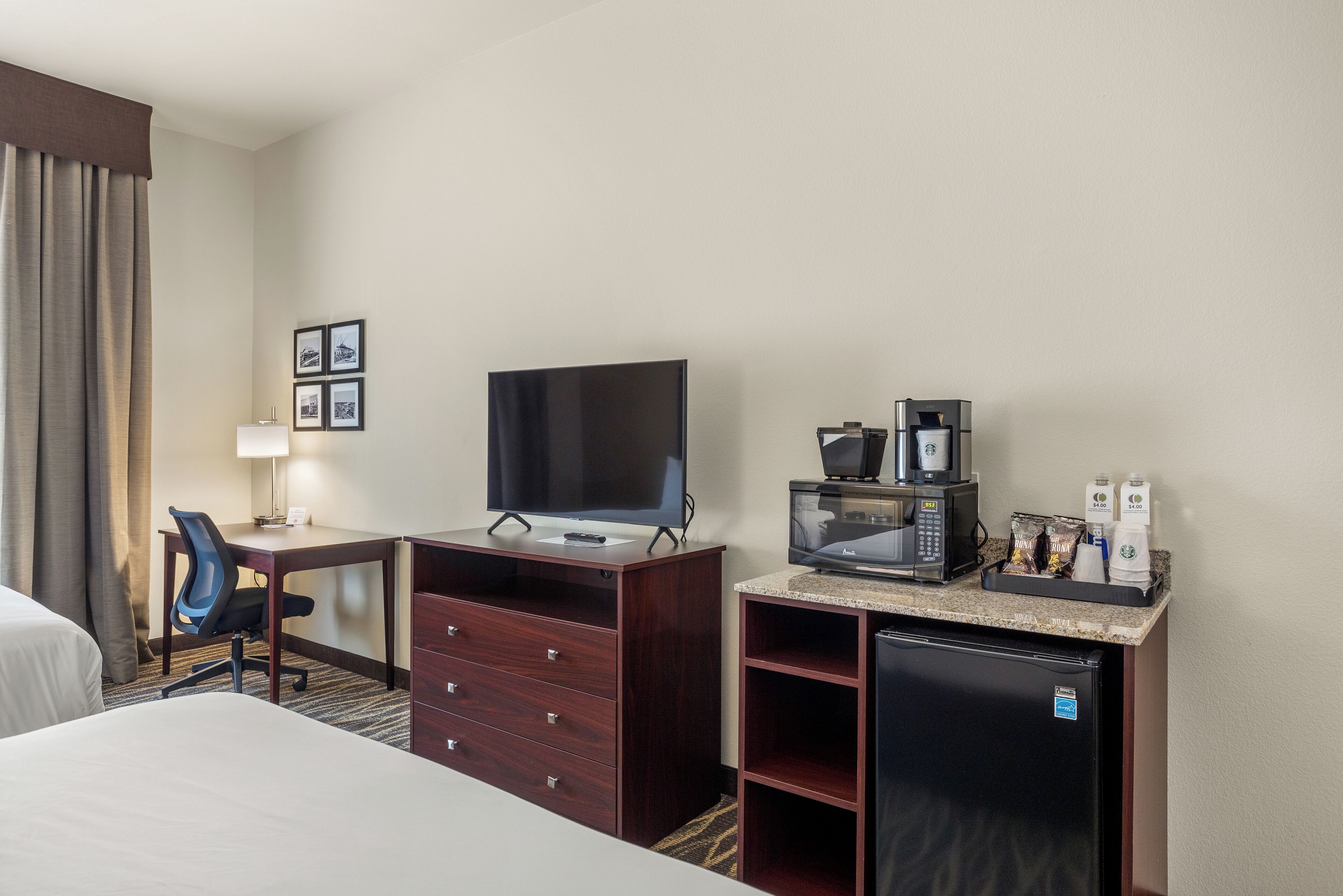 Ein Hotelzimmer mit Bett, Schreibtisch mit Computer, Fernseher, Kaffeemaschine und Kühlschrank.