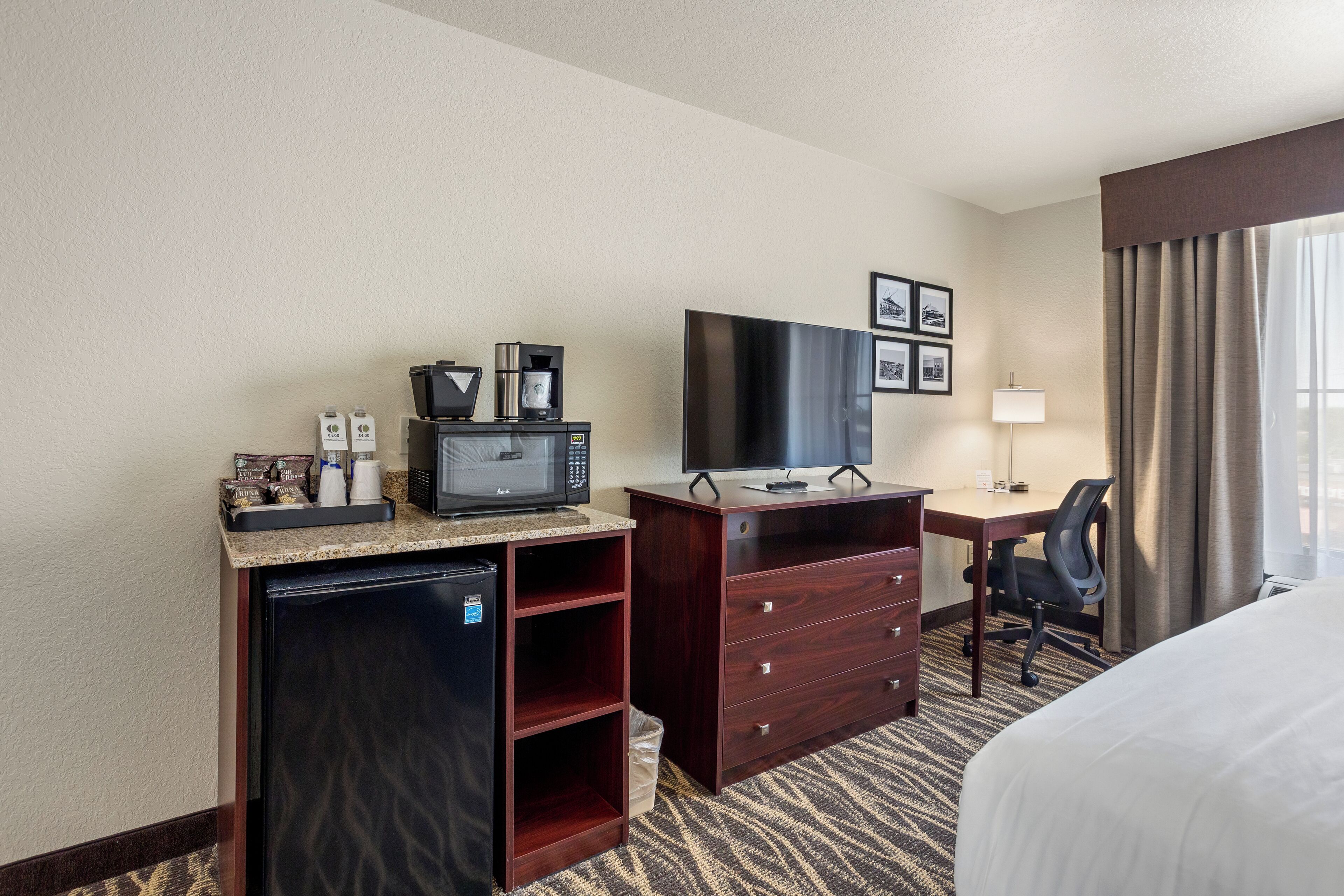 Een hotelkamer met een bed, een bureau met een computer en een televisie, een magnetron, een koelkast en een kleine prullenbak.