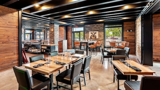 Un restaurante moderno con paredes de madera y techos altos a la vista, con varias mesas y sillas para comer.