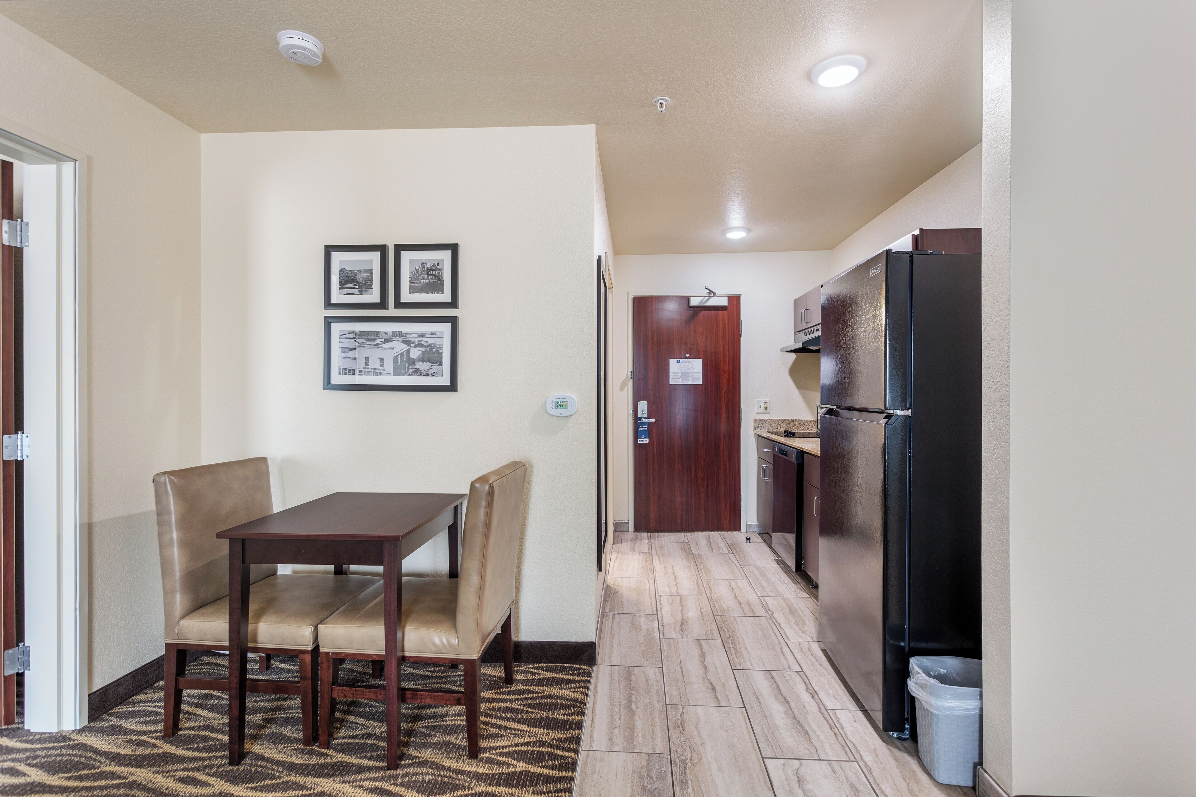 Una cocina compacta con comedor, que incluye una mesa y sillas, un refrigerador y una puerta con un cartel.