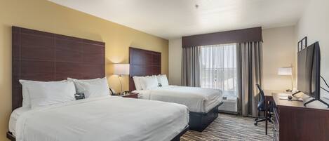 A hotel room with two beds, a desk, a chair, a TV, and a window with curtains.