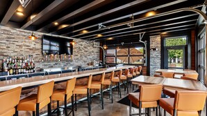 Una zona de bar con una barra larga, varios taburetes y una amplia variedad de botellas.