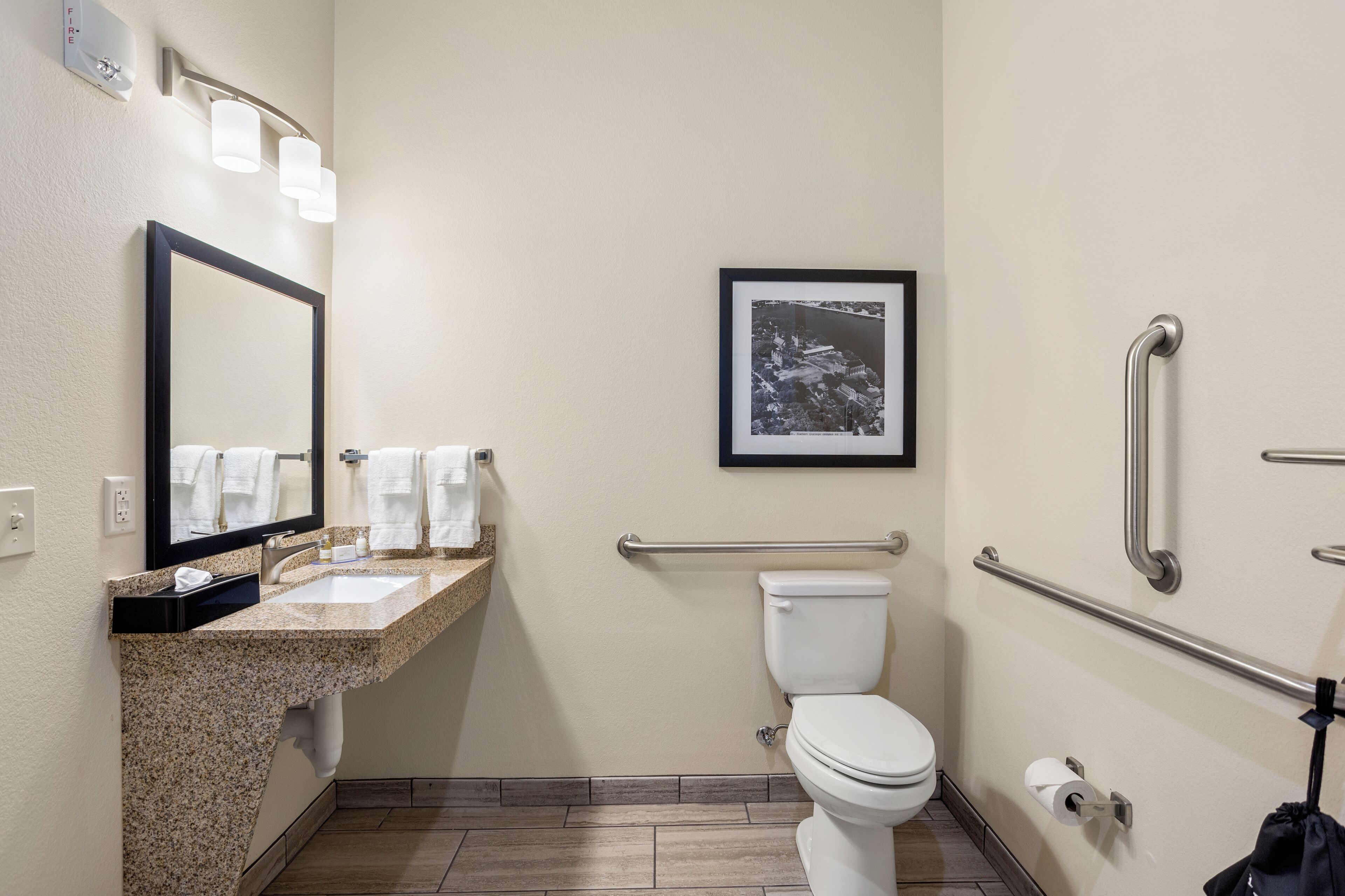 A bathroom with a sink, mirror, toilet, and handrails.