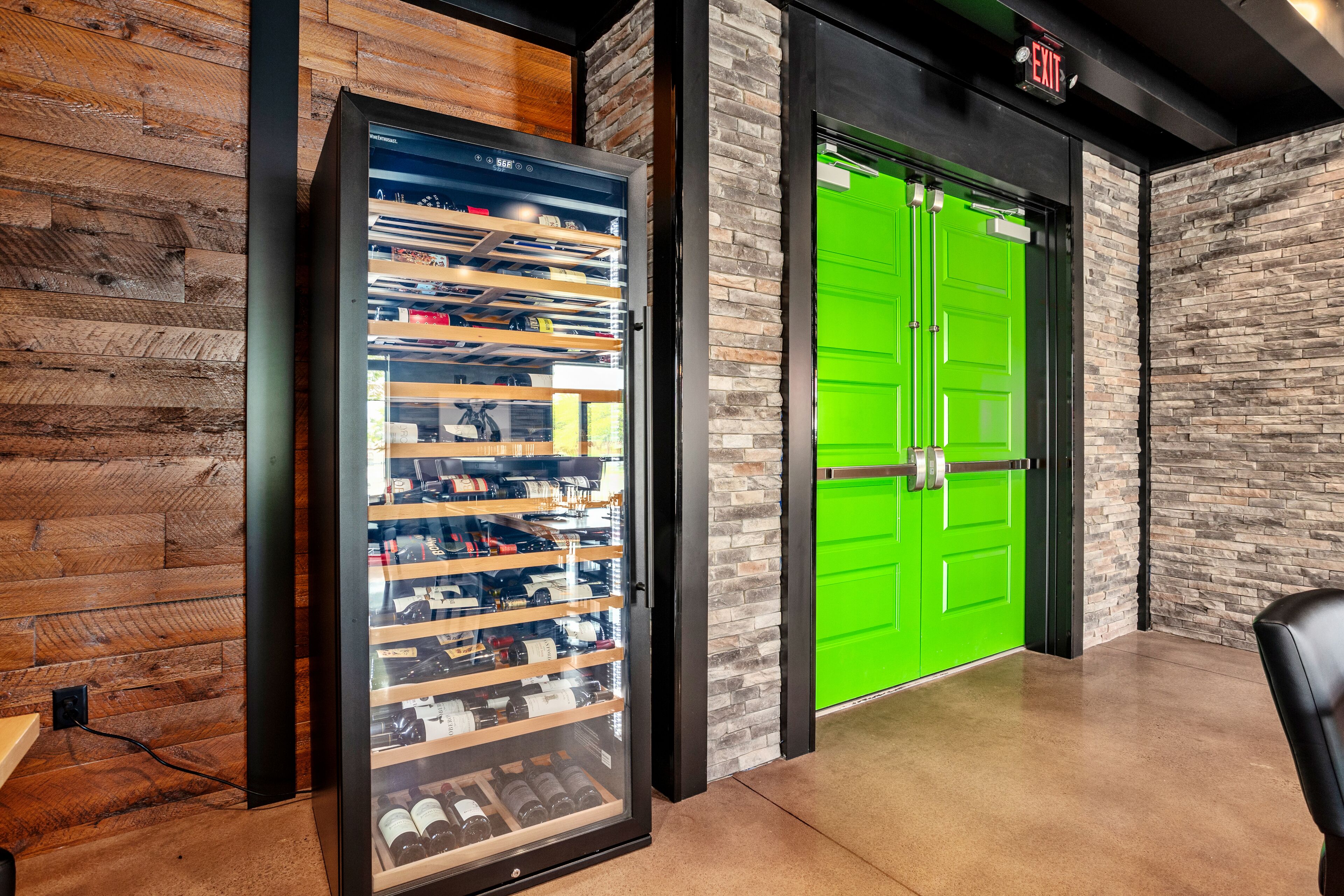 A modern interior with a wine cooler, a green door, and a black chair.