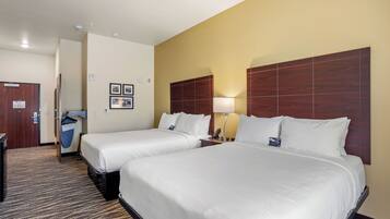 A hotel room with two beds, a desk, a trash bin, and a wall-mounted lamp.