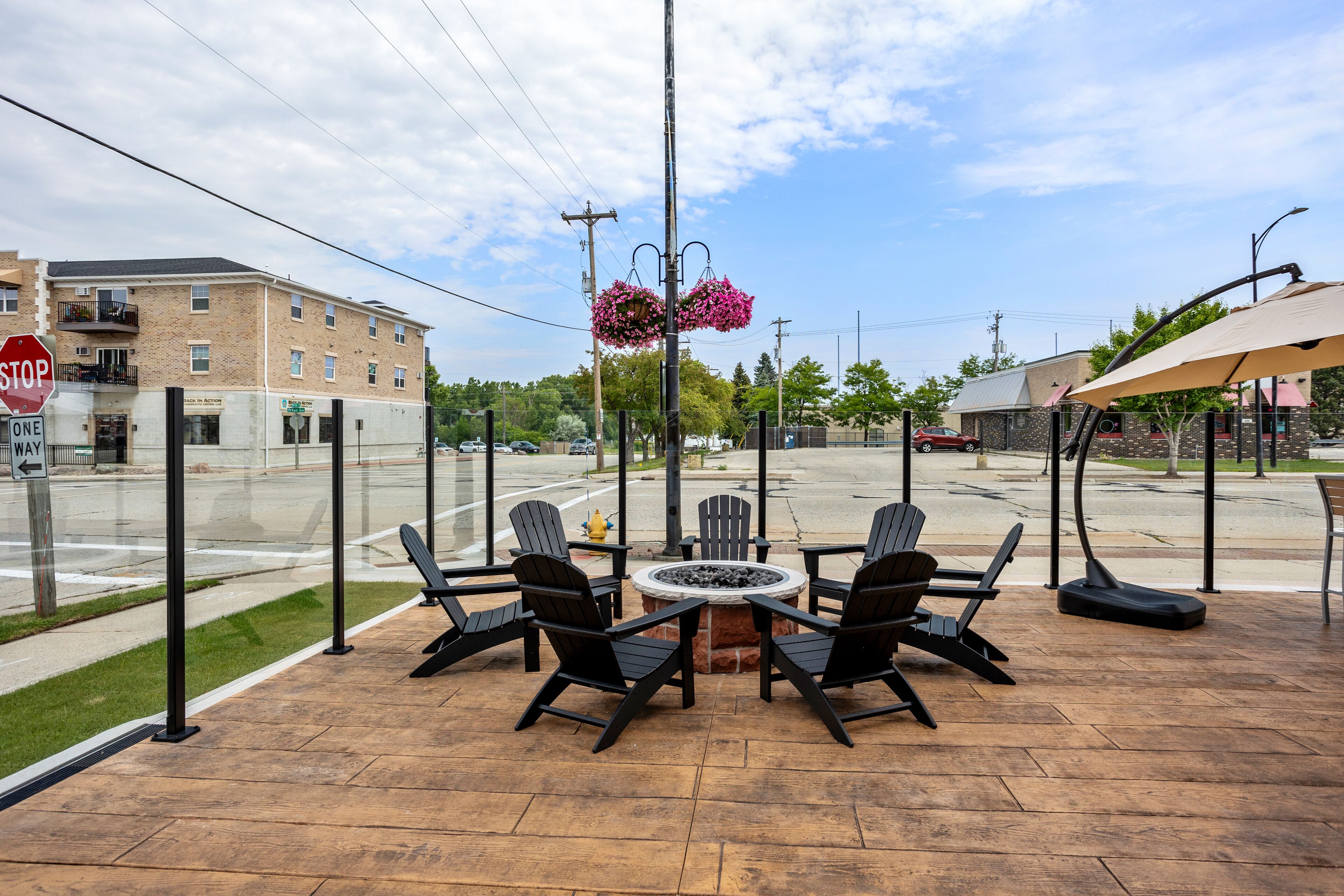 An outdoor patio with a fire pit, four Adirondack chairs, and hanging flower baskets.