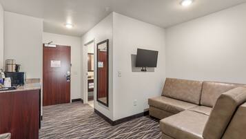 A hotel room with a kitchenette, a large mirror, a flat-screen TV, and a beige sofa.