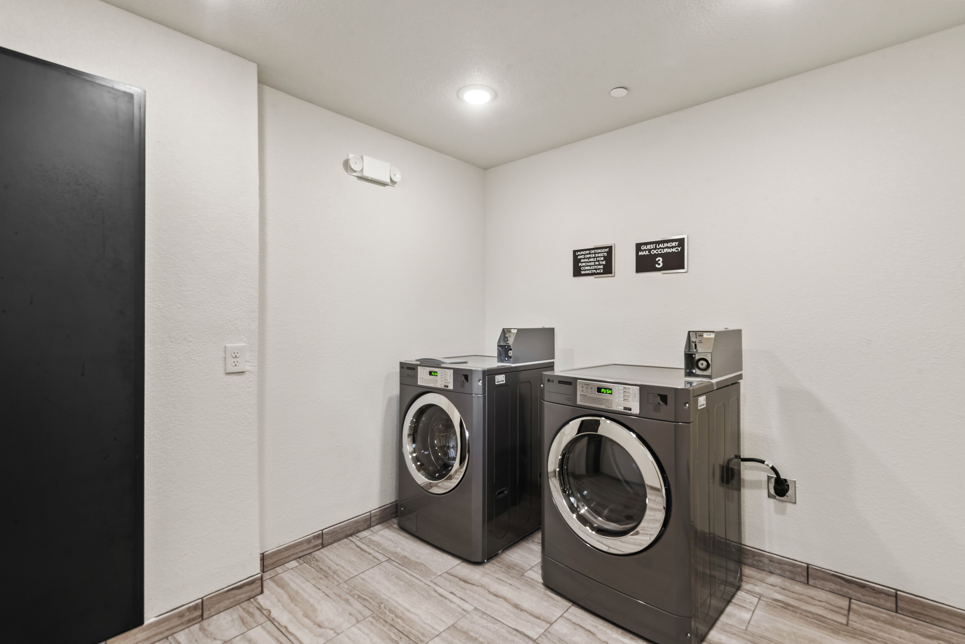 Une buanderie équipée de deux machines à laver à chargement frontal, d’un sèche-linge fixé au mur et d’une porte dotée d’un cadre noir.