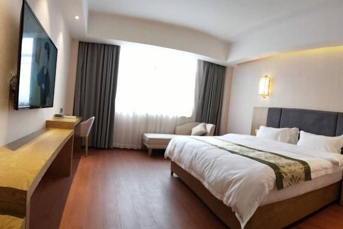 Habitación de hotel con cama, escritorio, silla, televisión y ventana con cortinas.