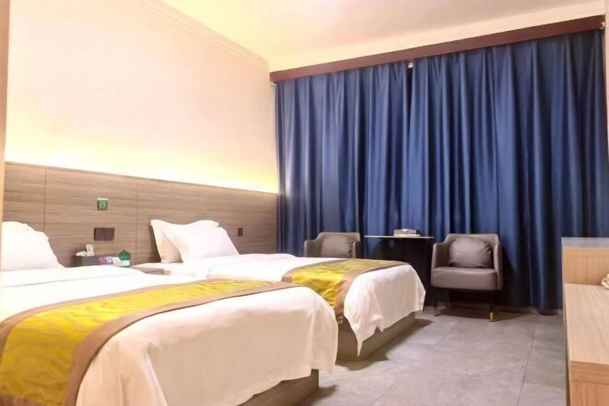 Habitación de hotel con dos camas, un escritorio, una silla y un ventanal con cortinas.