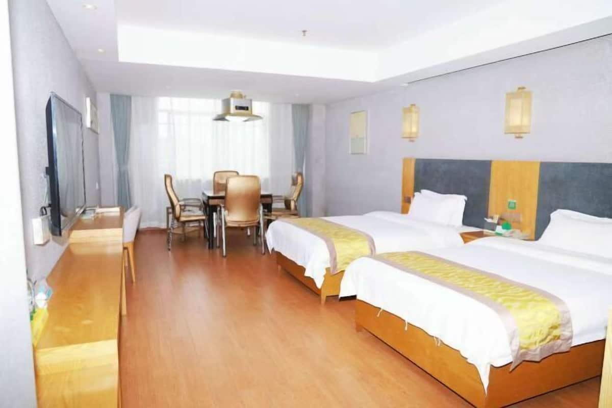 Una habitación de hotel con dos camas, una mesa de comedor con sillas, un televisor y una ventana con cortinas.