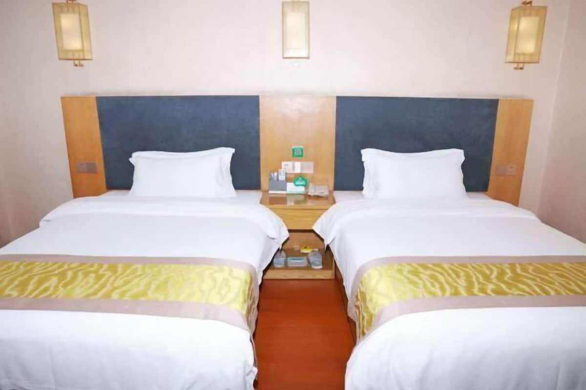 Habitación de hotel con dos camas, cabecero de madera, mesita de noche con lámpara y una pequeña mesa entre las camas.