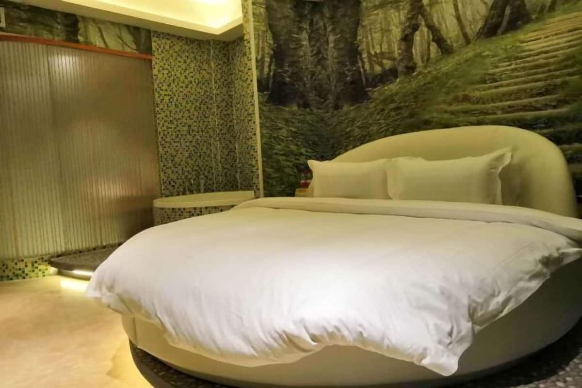 Una cama con cabecera blanca y almohadas, una pared con diseño estampado en verde, y un mural de una ladera boscosa.