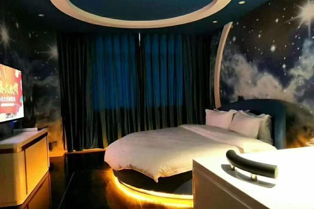 Un dormitorio con una cama, un televisor y un mural con un cielo nocturno en la pared.