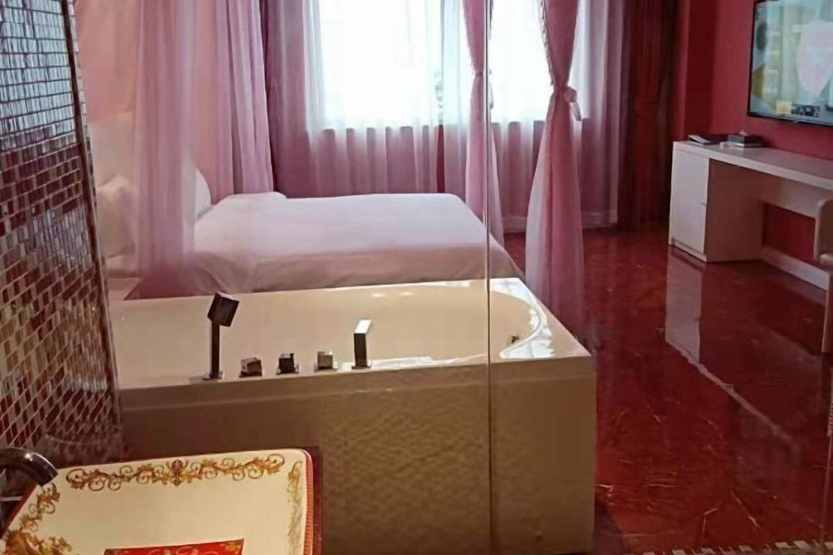 Habitación de hotel con cama, espejo grande, tocador con lavabo y televisor sobre un soporte.