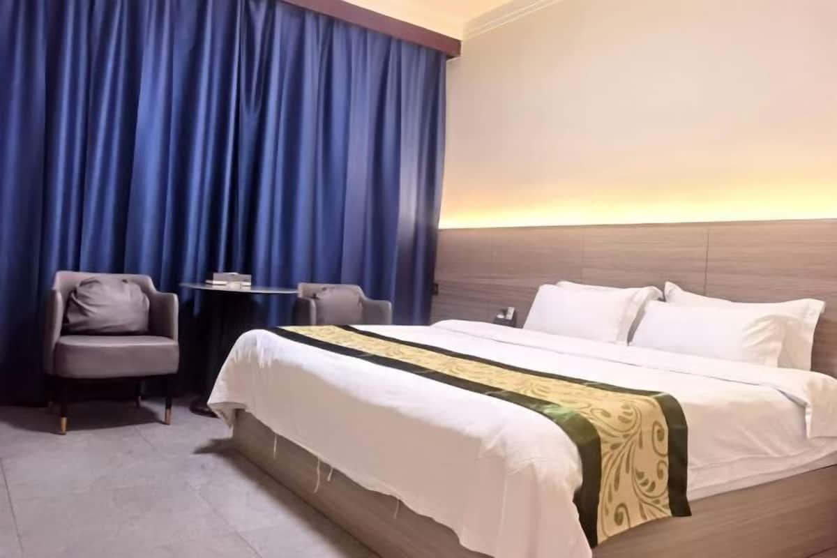 Habitación de hotel con una cama grande, una silla, una mesita y vista al atardecer.