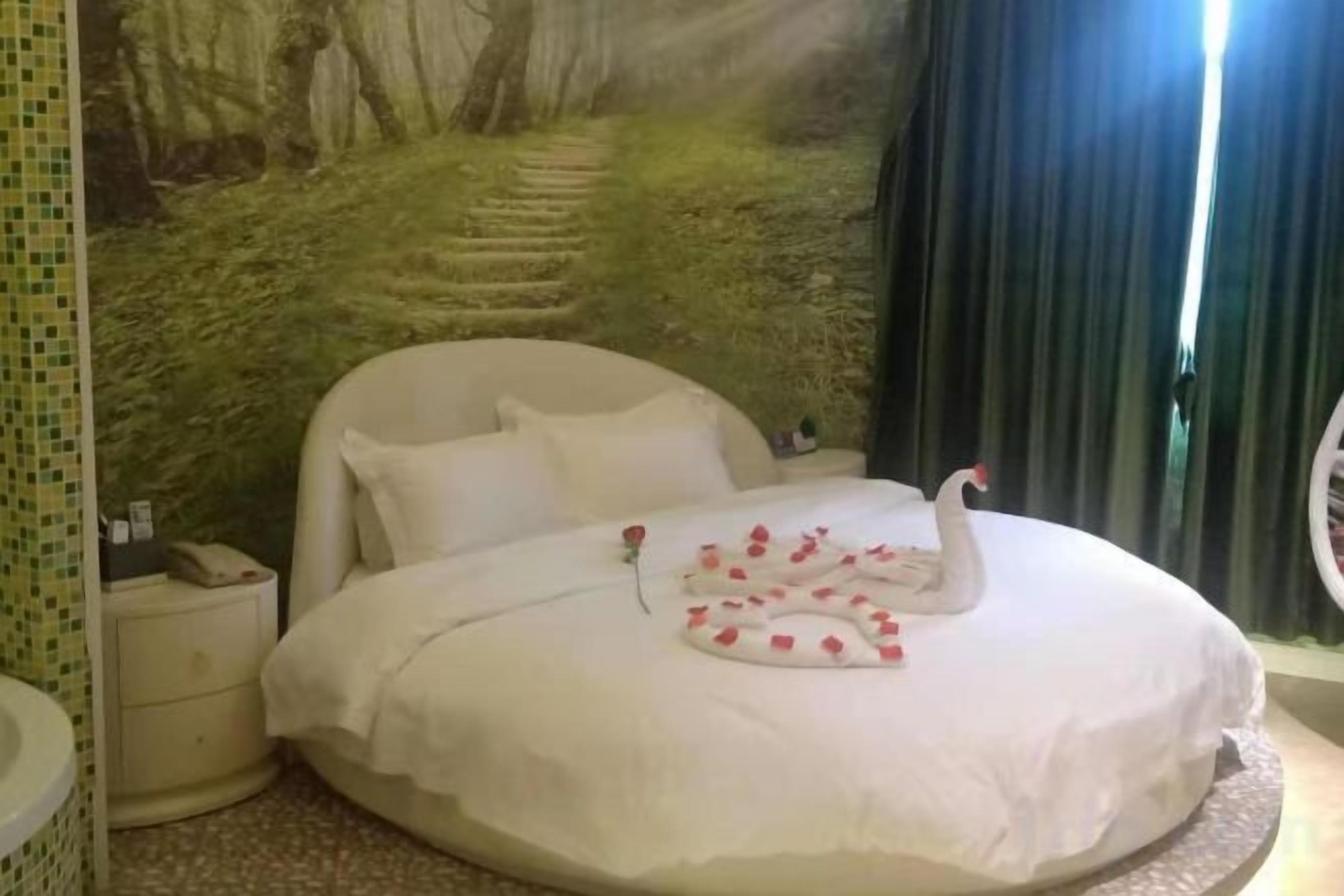 Una cama con decoración de cisne, una mesita de noche y un mural en la pared.