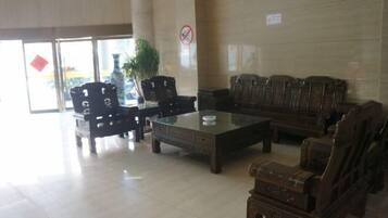 A lobby with a glass coffee table, wooden chairs, and sofas.