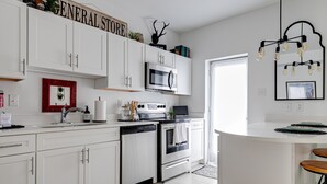 Una cocina moderna con armarios blancos, microondas integrado, lavavajillas y estufa. Un cartel sobre los armarios dice 'GENERAL STORE'.