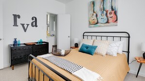 Un dormitorio con cama, cómoda, un cuadro de guitarras y una pared con letras.