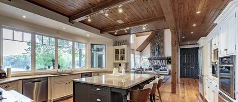 A spacious kitchen with a large island, wooden ceiling beams, and a stone fireplace.