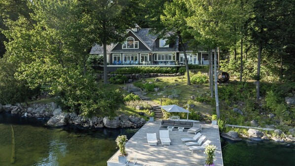 Une propriété au bord du lac, dotée d’un quai, de chaises longues et d’un sentier en pierre menant à une maison.