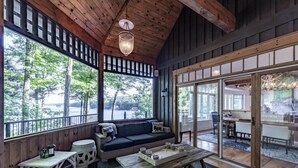 A cozy room with a wooden ceiling, large windows, a sofa, and a dining area.