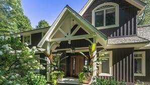 A two-story house with a covered porch and a garden with white hydrangea flowers.