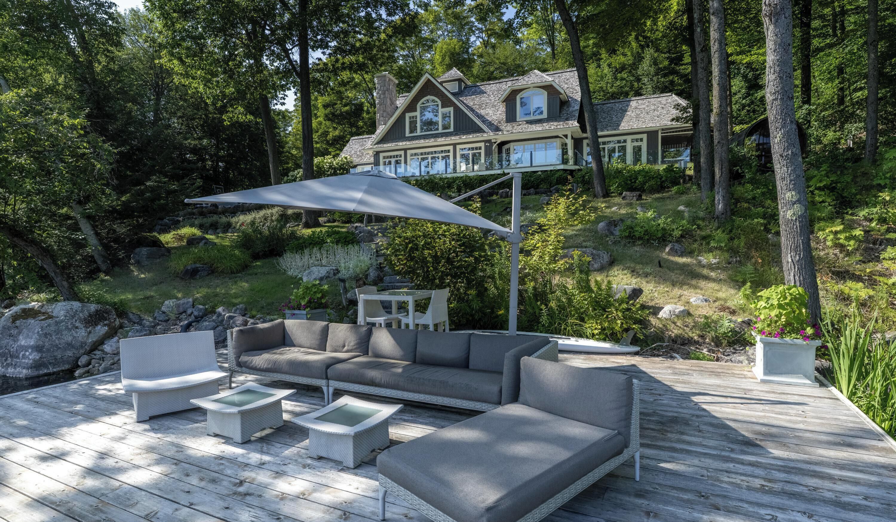 A deck with outdoor furniture, a large umbrella, and a house in the background.