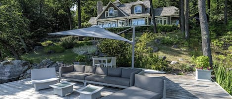 A deck with outdoor furniture, a large umbrella, and a house in the background.