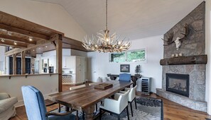 Un coin repas avec une table en bois, des chaises, un lustre et une cheminée en pierre.