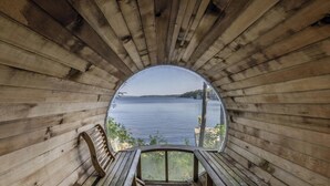 A wooden cabin with a circular window offering a view of a lake and distant land.