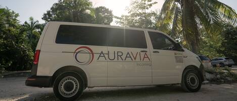 A white van with "AURAVIA" and "Incoming" on the side parked on a dirt road with palm trees in the background.