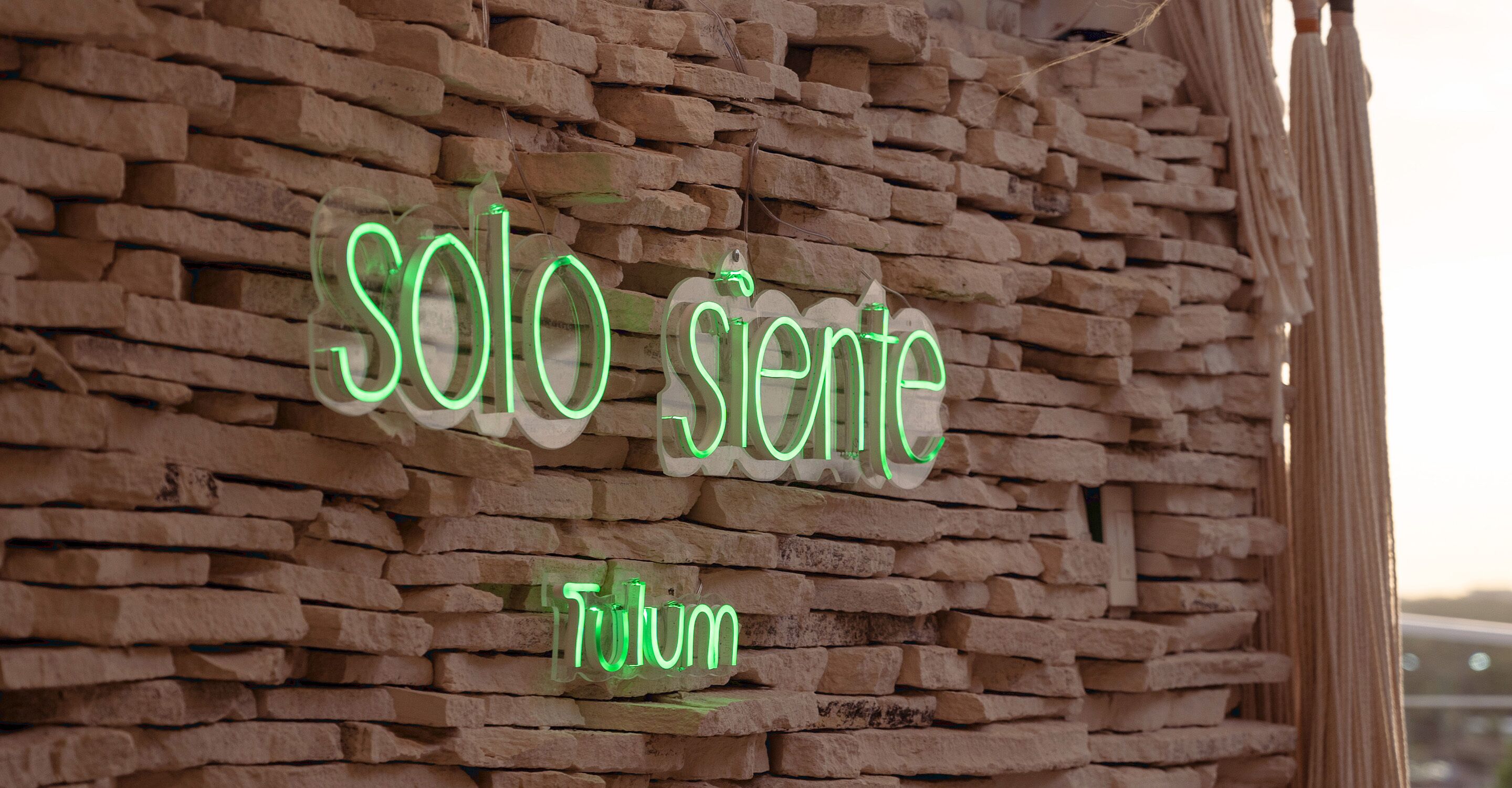 Une enseigne au néon avec les mots « solo siene » et « Tulum » sur un mur de briques.