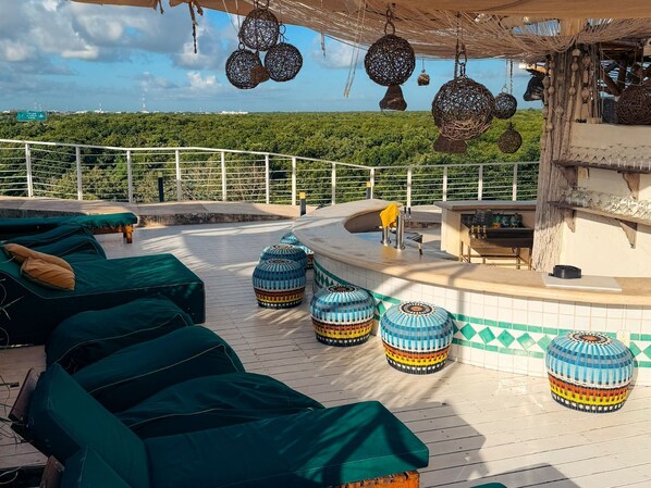 A rooftop terrace with lounge chairs, a bar area, and hanging decorative items.