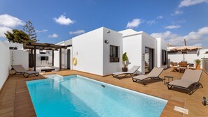 Un área moderna junto a la piscina con una piscina rectangular, tumbonas y un pequeño espacio de estar al aire libre.